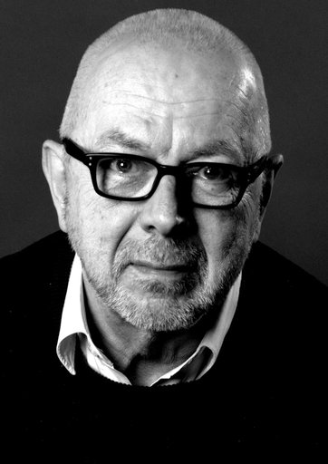 A black and white photograph of a bald man wearing glasses.
